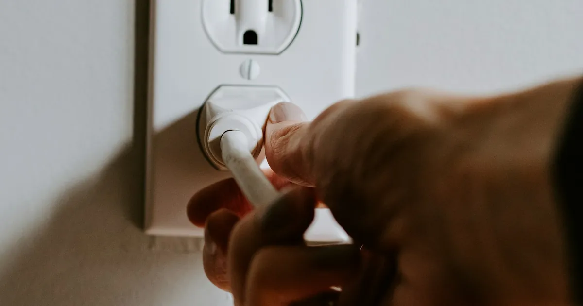 壁のコンセントへ白い電源プラグを差す手元
